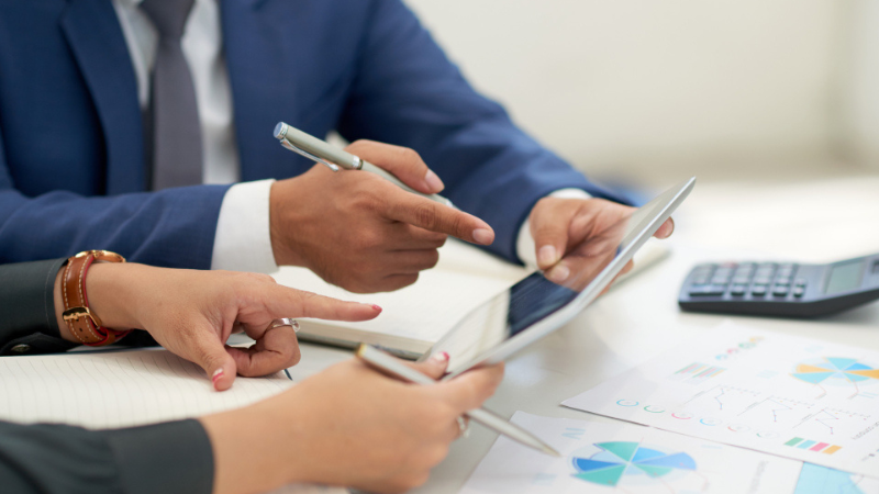 Business professionals reviewing financial charts and data on a tablet to discuss Corporate Tax in Oman requirements.